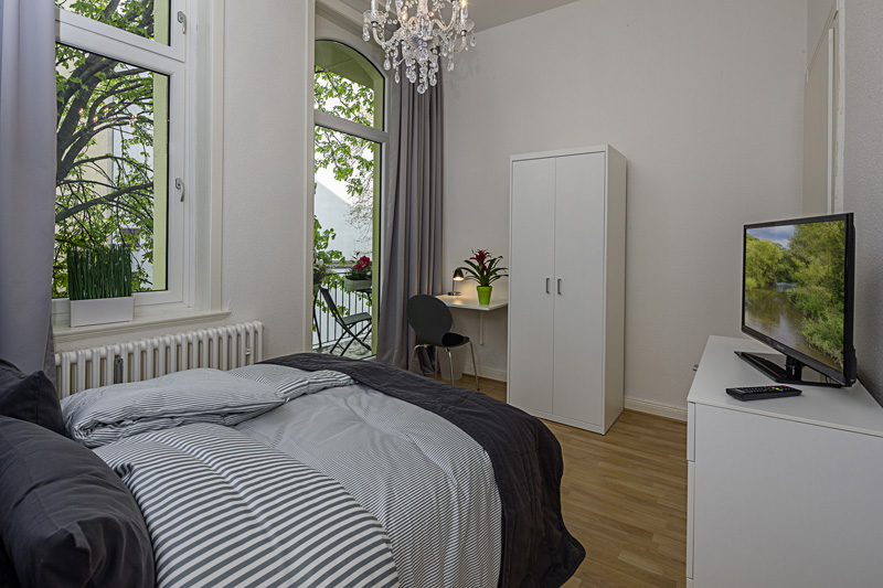 Weißes Schlafzimmer mit einem Laminatboden und einem Doppelbett gegenüber eines weißen Schrankes