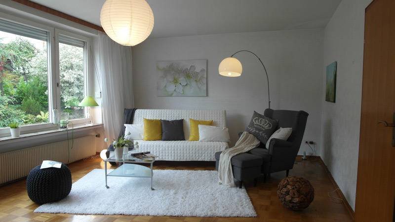 Weißes Wohnzimmer mit Laminatboden, einer Couch mit Couchtisch und einem Sessel