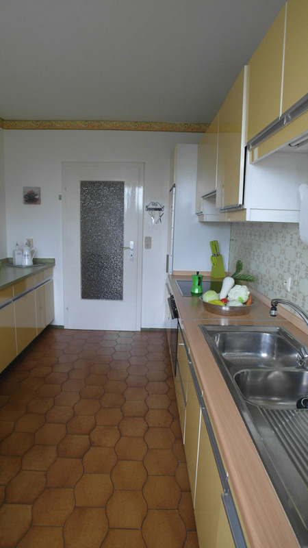 Weiße Küche mit braunem Boden und einer senfgelben Küchenzeile