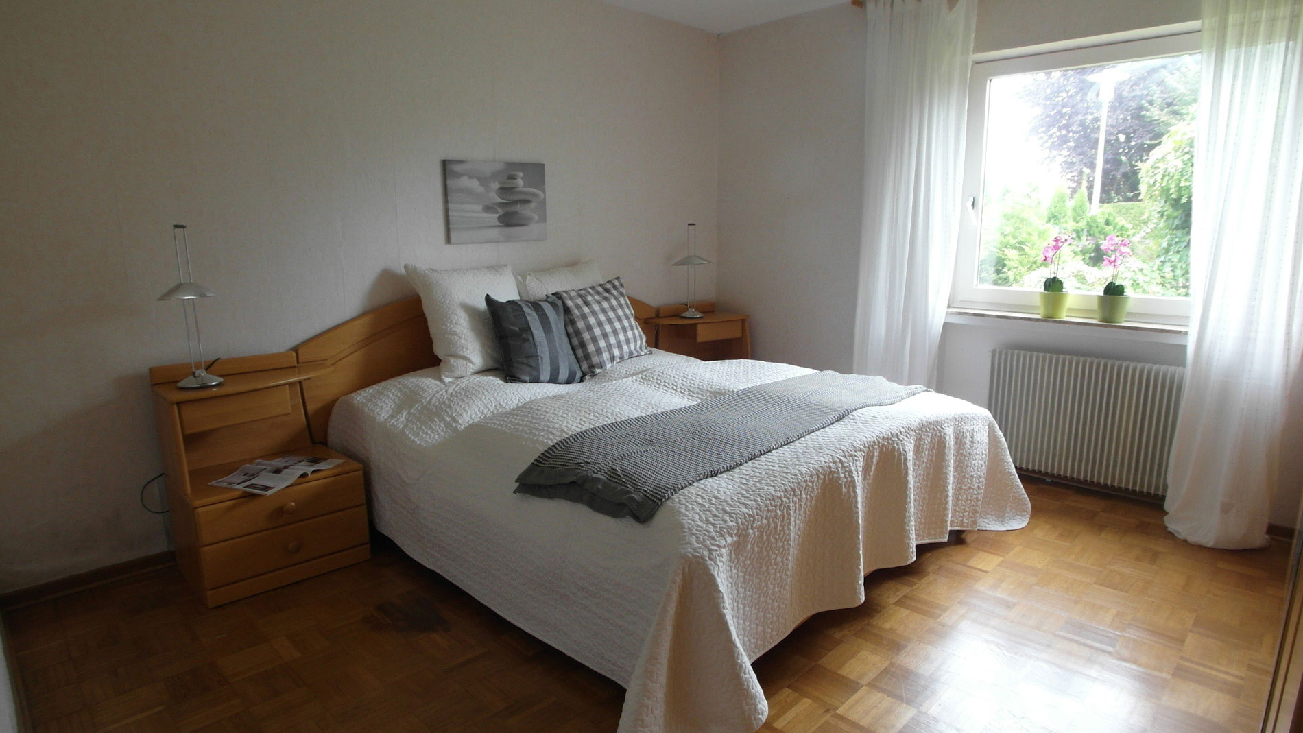 Weißes Schlafzimmer mit Parkettboden und einem Doppelbett mit dazugehörigen Holz-Nachttischen