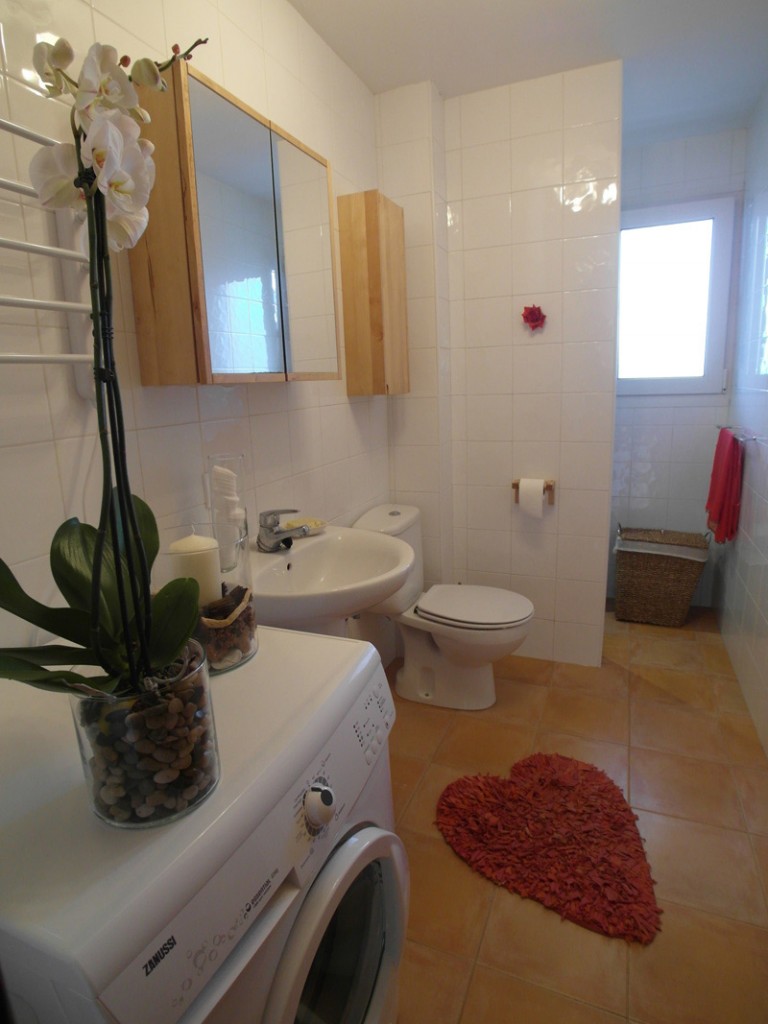 Weißes Badezimmer mit braunen Bodenfliesen und einem herzförmigen Teppich