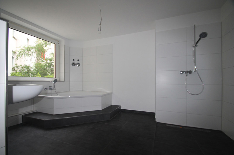 Weißes Badezimmer mit dunkelgrauem Boden und einer Eckbadewanne mit Stufe