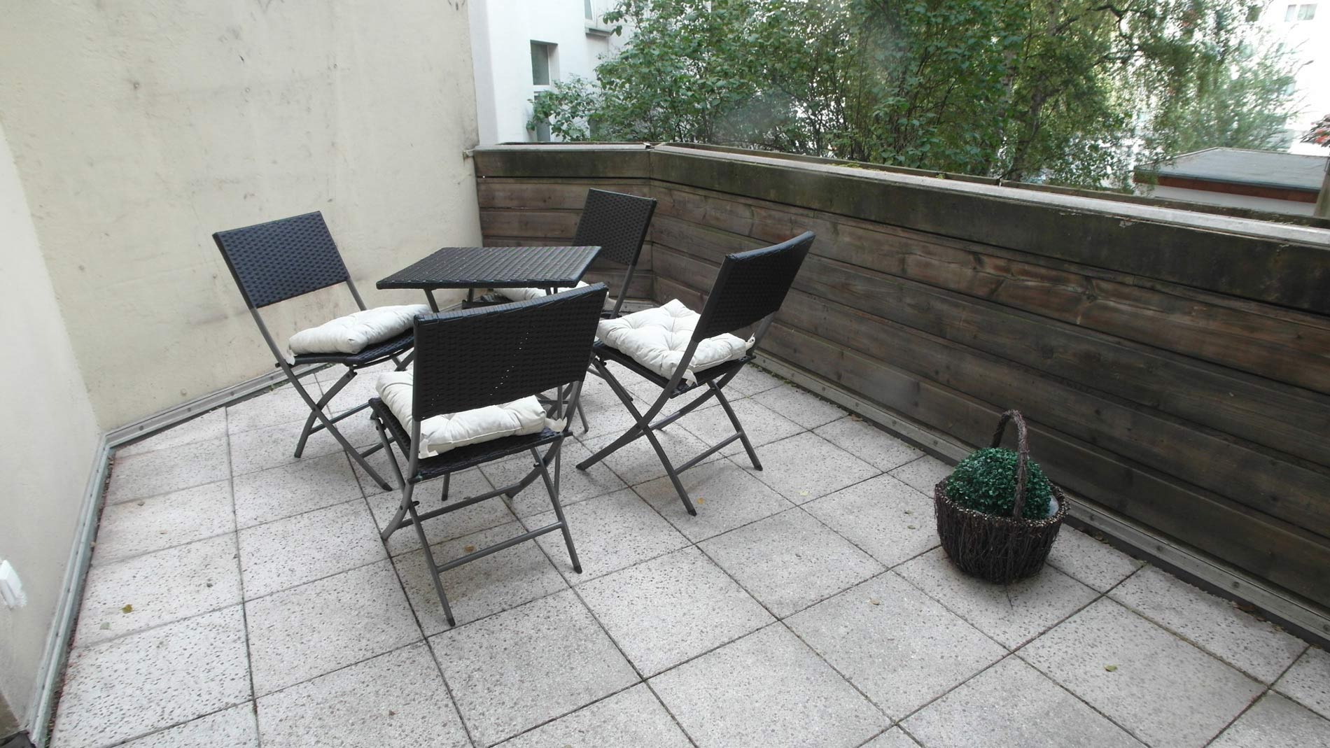 Balkon mit hellen Steinplatten und anthrazitfarbenen Gartenmöbeln