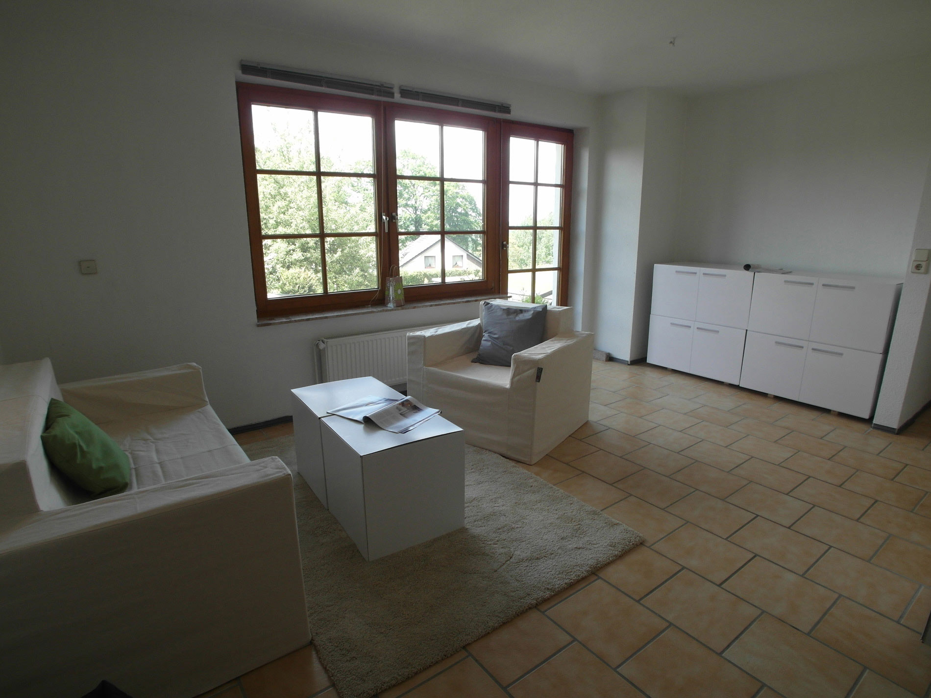 Weißes Wohnzimmer mit braun-beigen Bodenfliesen und einer Holz-Fenstertür