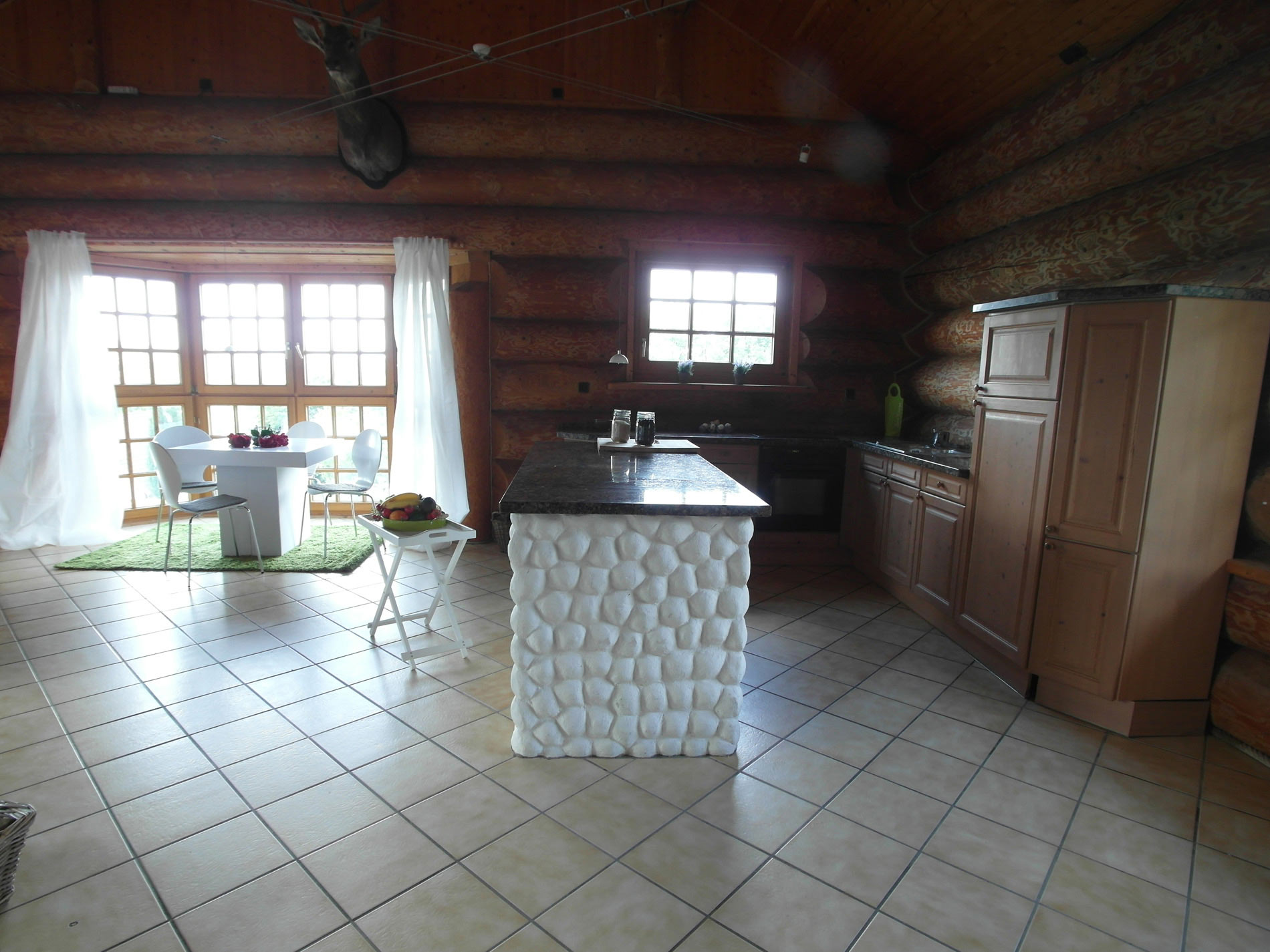 Rustikale Küche mit einem weißen Naturstein Tresen und Baumstamm-Wänden